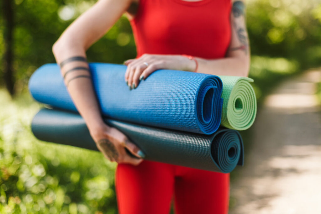 close-up-photo-young-woman-body-red-jumpsuit-standing-with-colorful-yoga-mats-hands-park